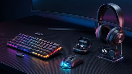 A sleek gaming setup with a colorful RGB keyboard, illuminated mouse, wireless earbuds, and headphones on a black surface, conveying a modern tech vibe.