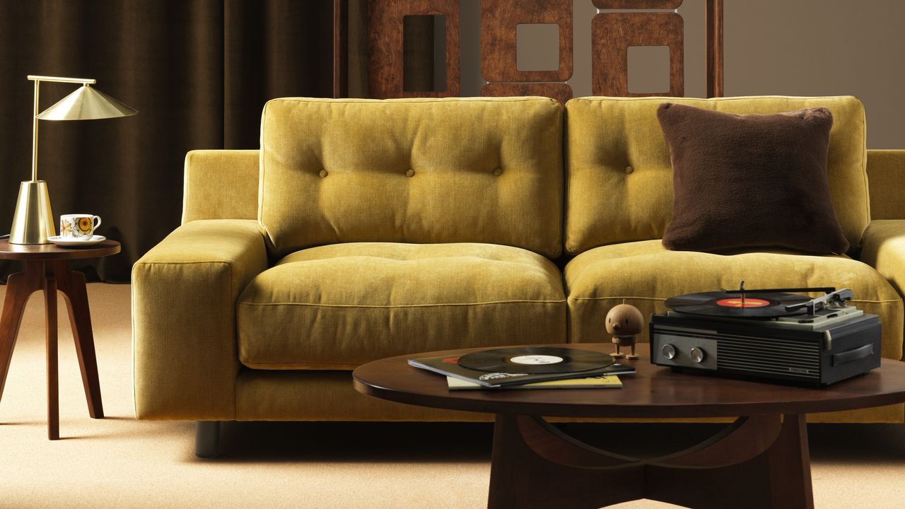 A yellow Habitat sofa in a dark living room with a round mid-century modern coffee table