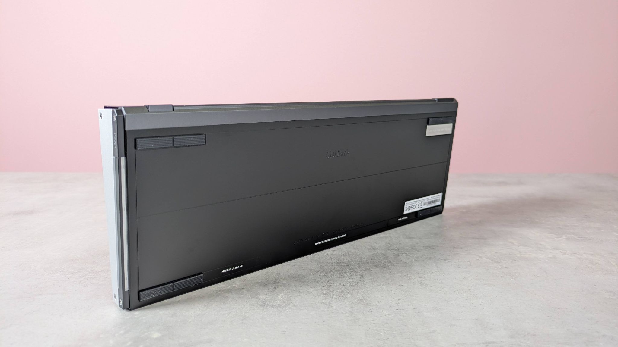 Underside view of MelGeek Made68 Ultra V2, standing up on desk with pink wall in background