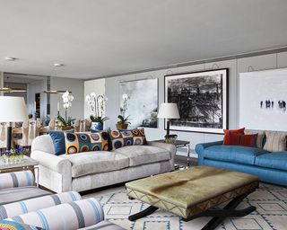 A gray apartment living room with blue sofa, gold ottoman and primary colored accents along with a mirrored wall and large modern art works.