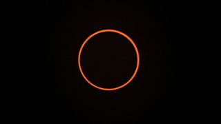 A thin orange band circles a round black shadow as the moon covers most of the sun during the Oct. 14 eclipse