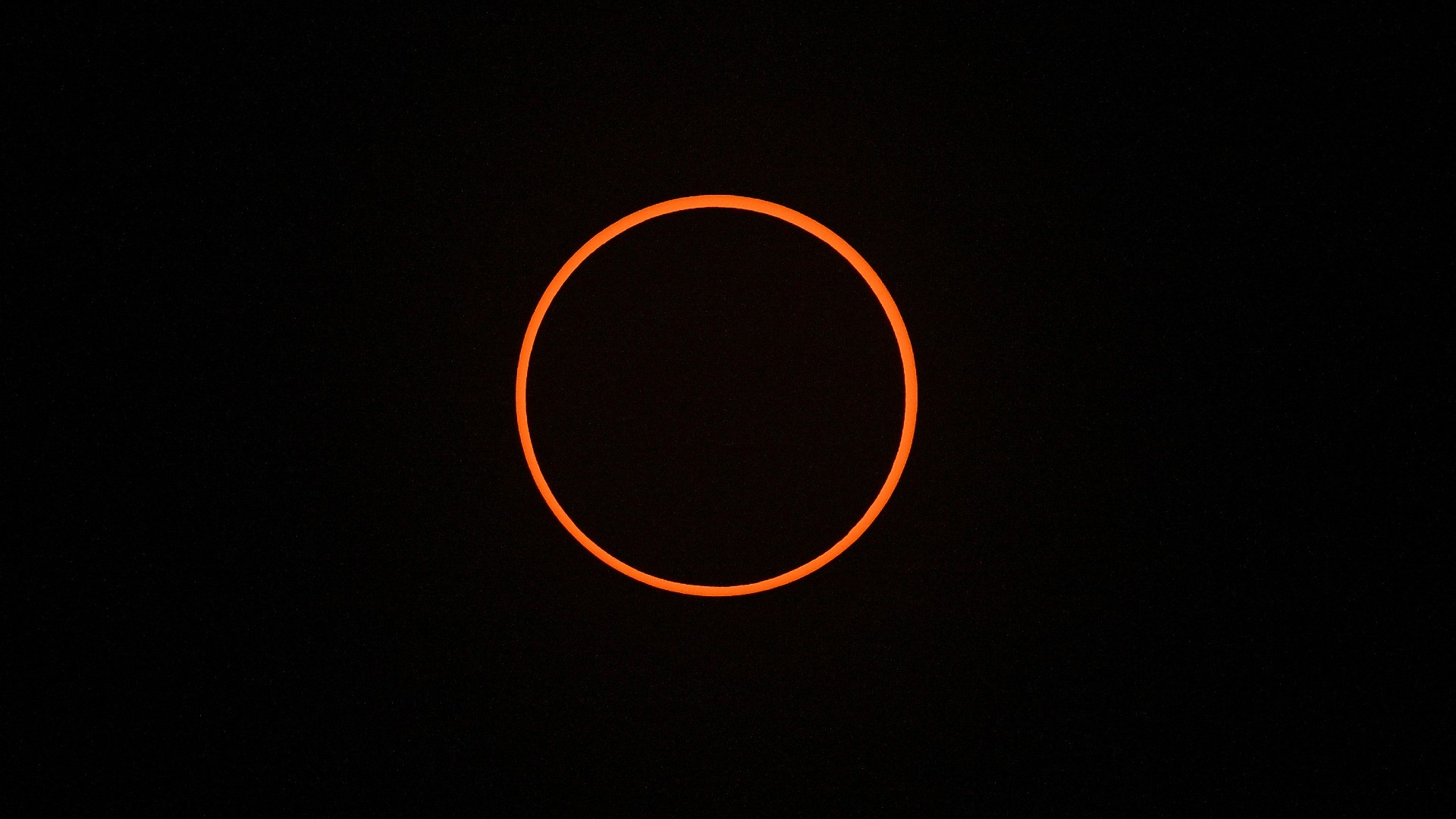 A thin orange band circles a round black shadow as the moon covers most of the sun during the Oct. 14 eclipse