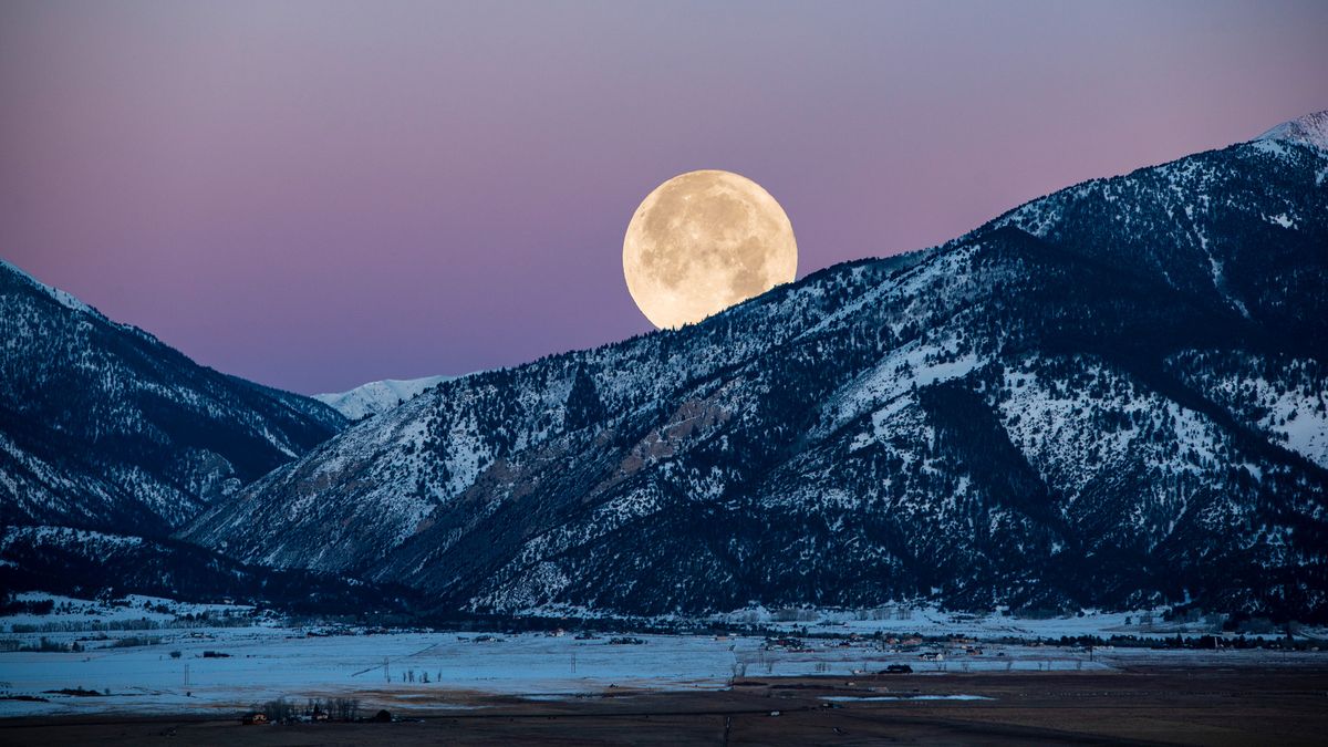 full moon rising over a snowy mountain
