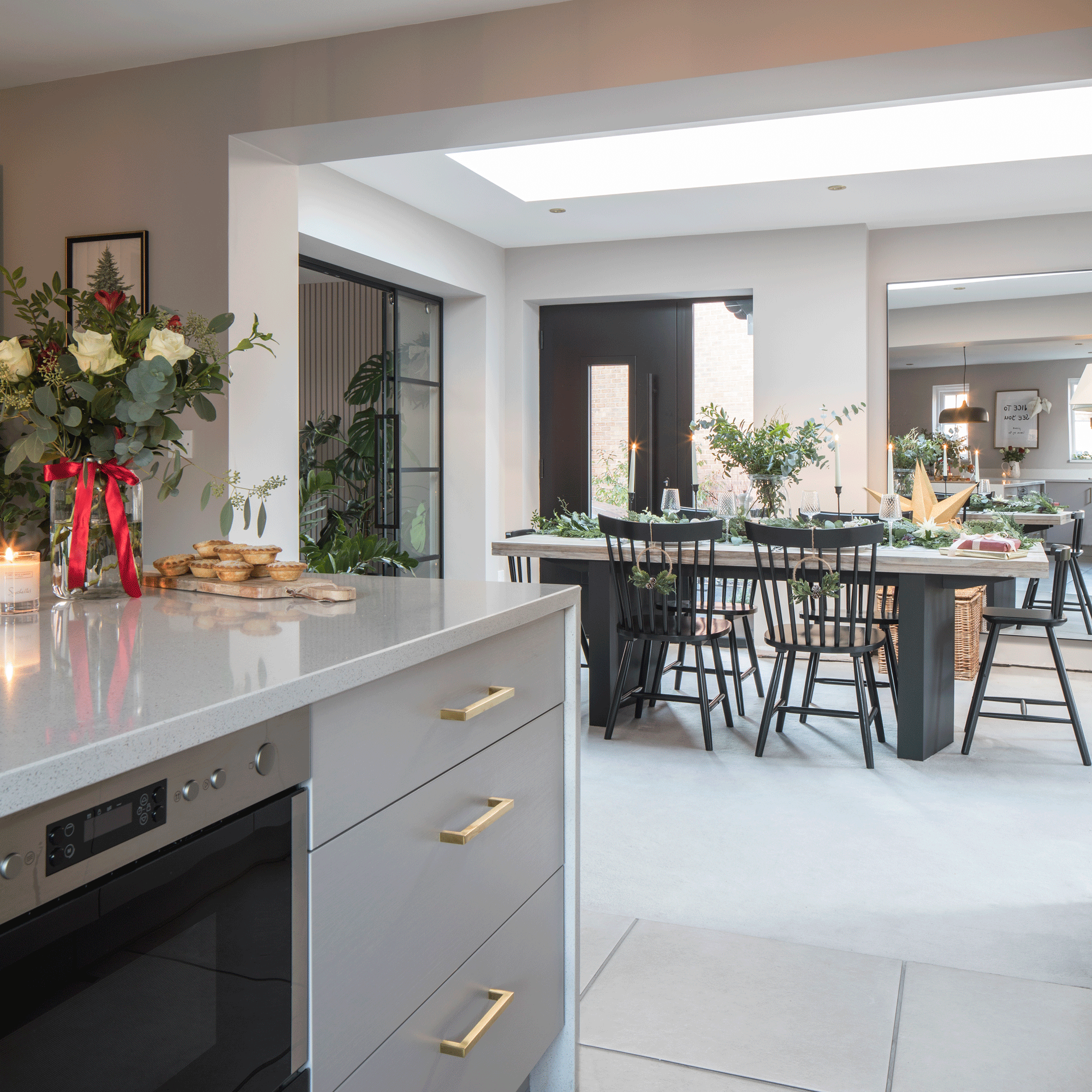a white contemporary kitchen with a view into an open plan din ing area, all decorated for Christmas