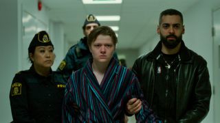 Dogge (Olle Strand) in a dressing grown being escorted by Farid (Ardalan Esmaili, right) and other police officers in Deliver Me episode 1