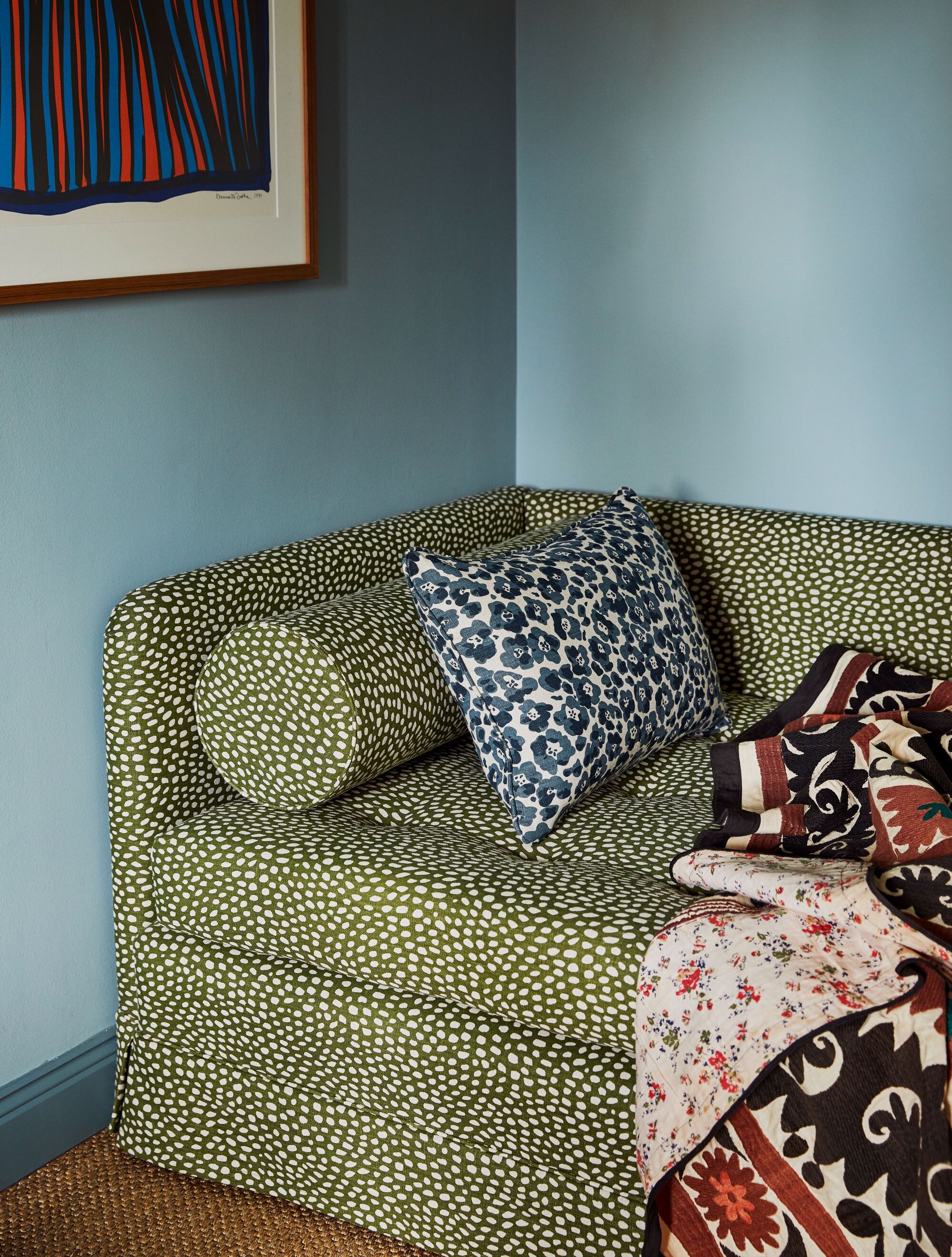 green patterned polka dot sofa in front of blue wall with artwork, patterned cushion and patterned blanket