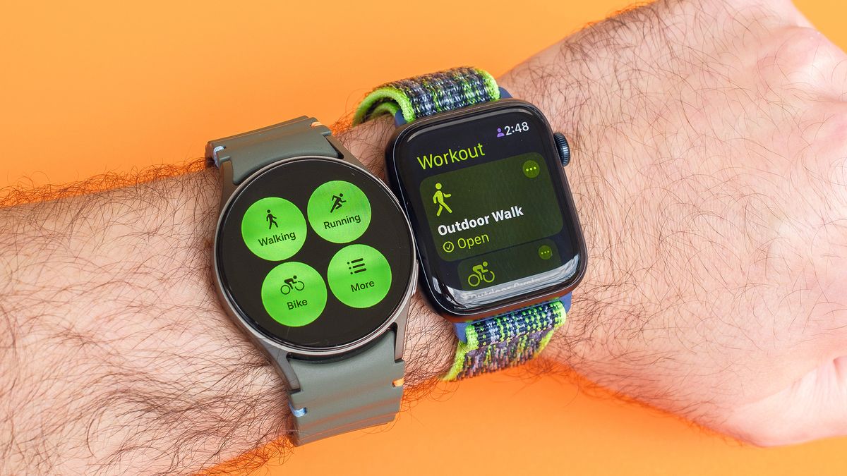 Close up of a Samsung Galaxy Watch 7 and Apple Watch SE 2022 on a user&#039;s wrist with the fitness app opened on each 