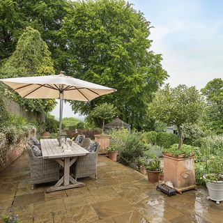 garden with dinning table chairs and umbrella plants and stone flooring