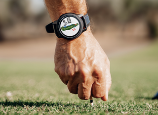 GolfBuddy watch on wrist as man tees up ball