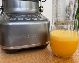 A glass of orange juice made using the Sage 3X Bluicer on wooden dining table