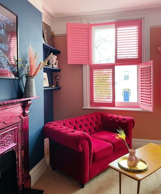 A pink small living room with a pink couch, fireplace, and a wooden coffee table