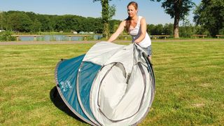Person folding a Coleman pop-up tent in a field