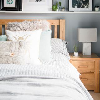 bedroom with grey color wall and wooden bed with lamp on bedside table and cushions on bed
