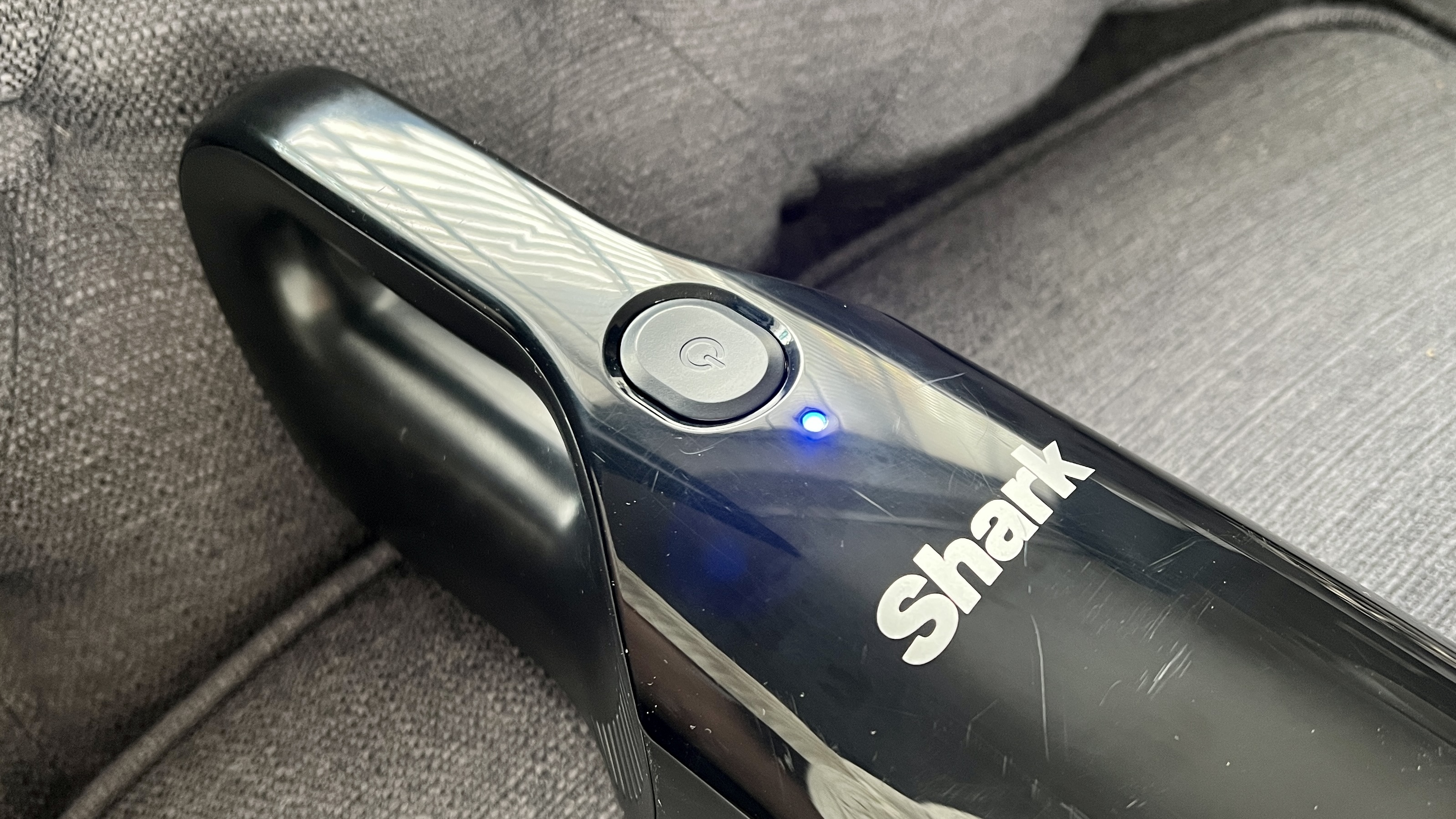 Tombol daya pada penyedot debu genggam Shark UltraCyclone Pet Pro Plus dengan lampu yang menunjukkan penyedot debu menyala