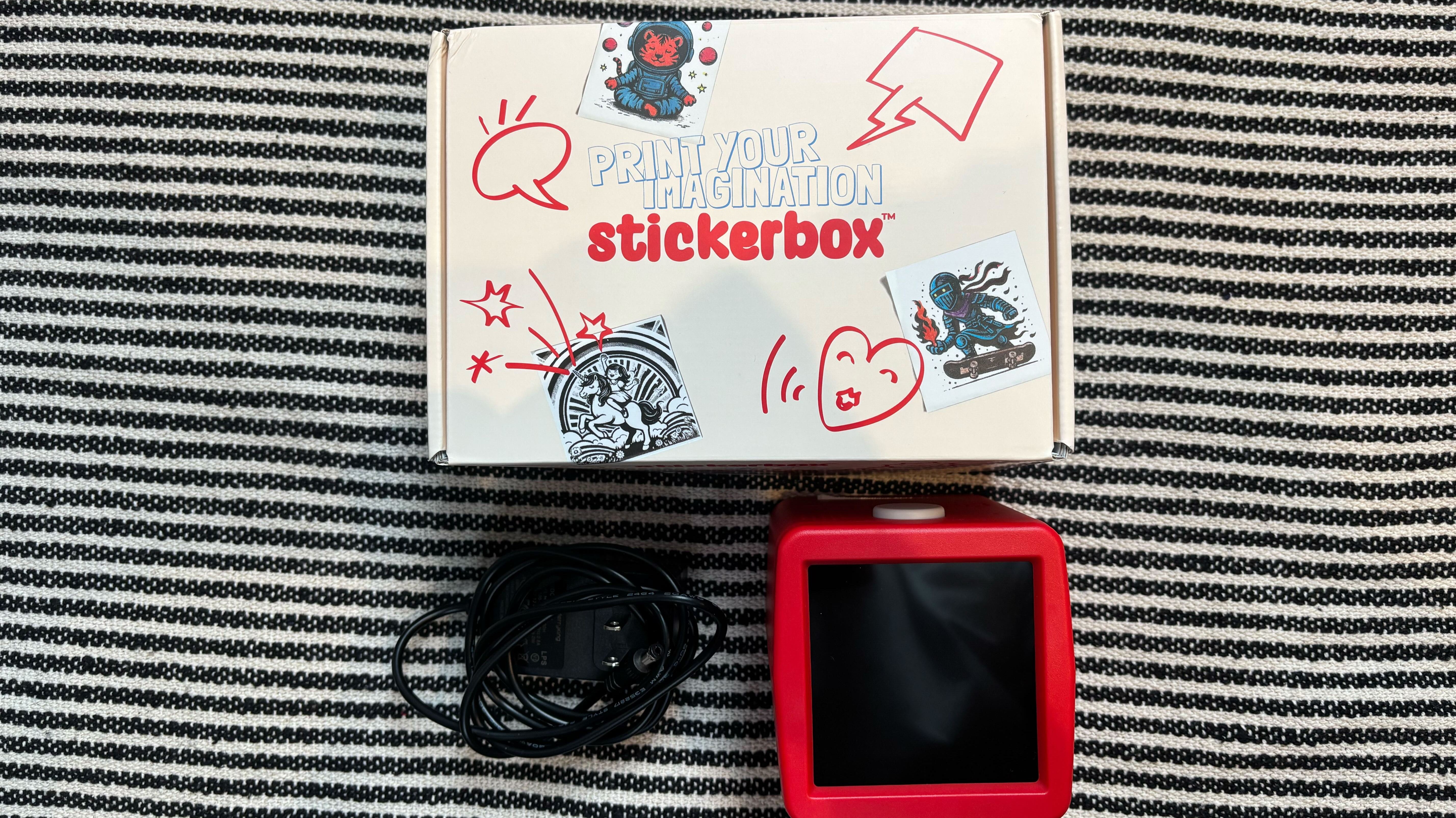 The Stickerbox device out of its packaging next to its plug-in cable