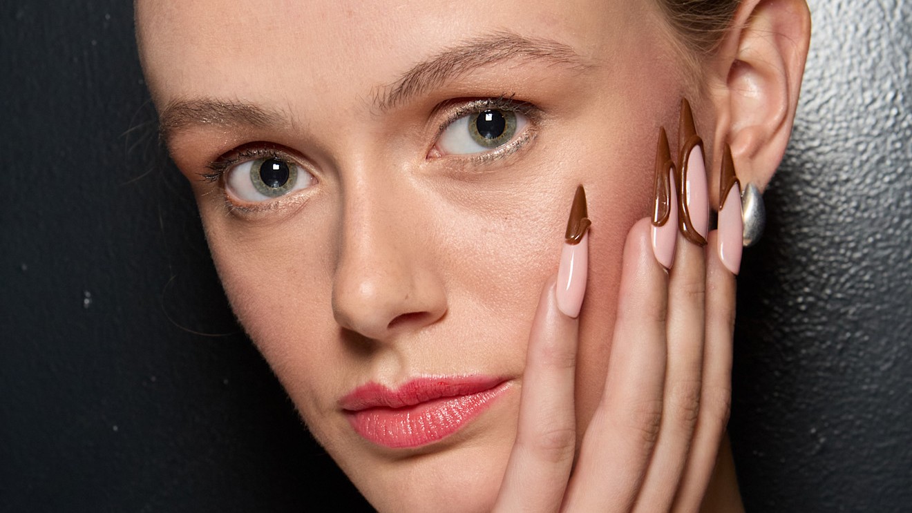 girl with blue eyes who has her hand and almond manicure resting on her face