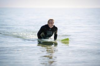 Sean (Peter O'Brien) out in the ocean, lying on his surfboard, wearing a wetsuit