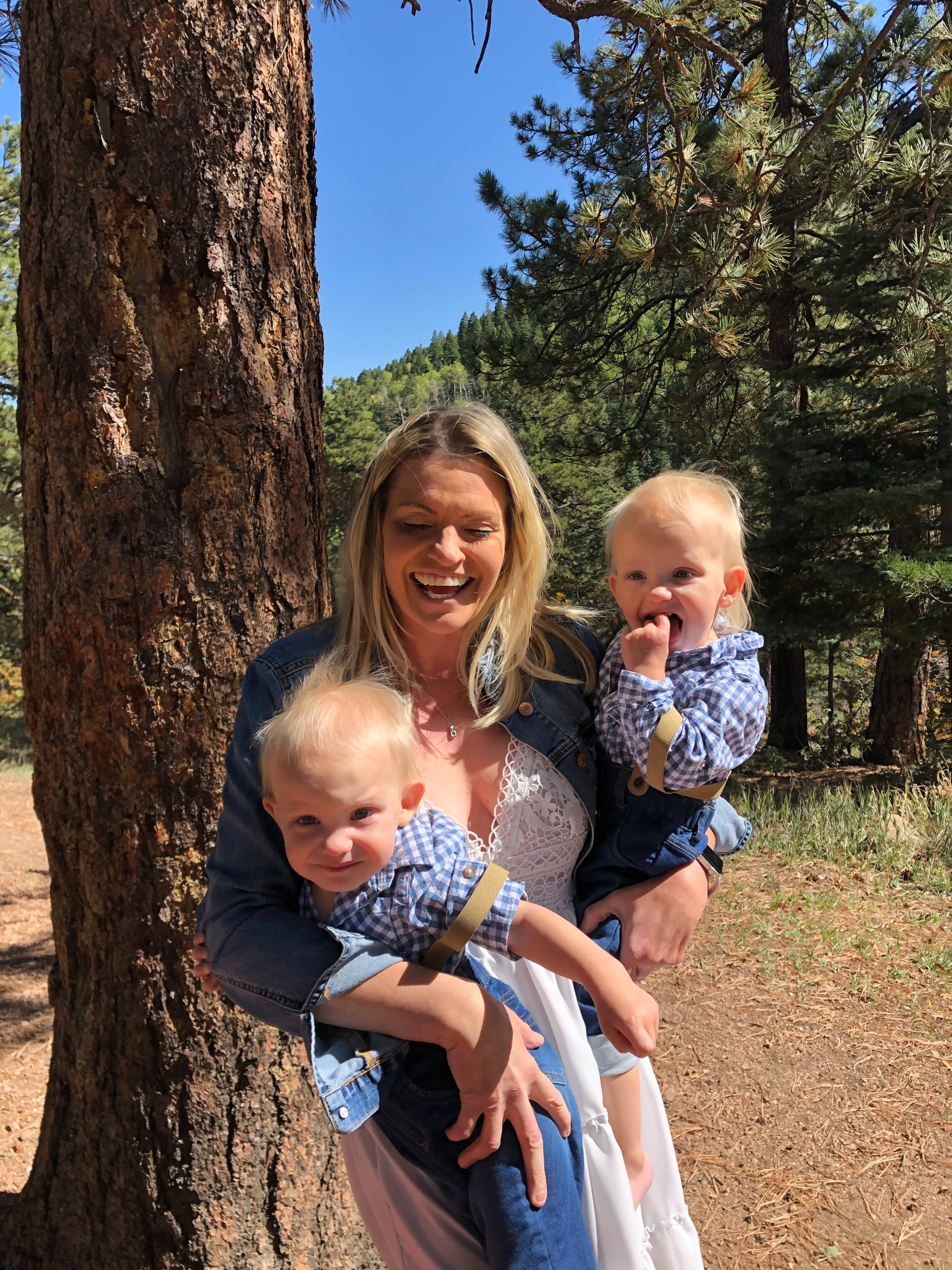 Monica Andreasen holds her young twin sons outdoors in a wooded area.