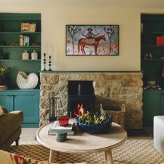 sitting room in cottage with stone fireplace and built-in cupboards in alcoves painted teal