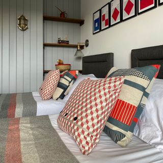 coastal bedroom ideas with twin beds, tongue and groove walls, bulkhead lights, artwork, shelving, stripe and graphic print cushions
