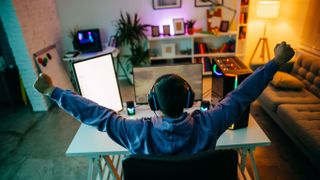 A PC Gamer sitting at a desk with his back to the camera with both arms in the air cheering.