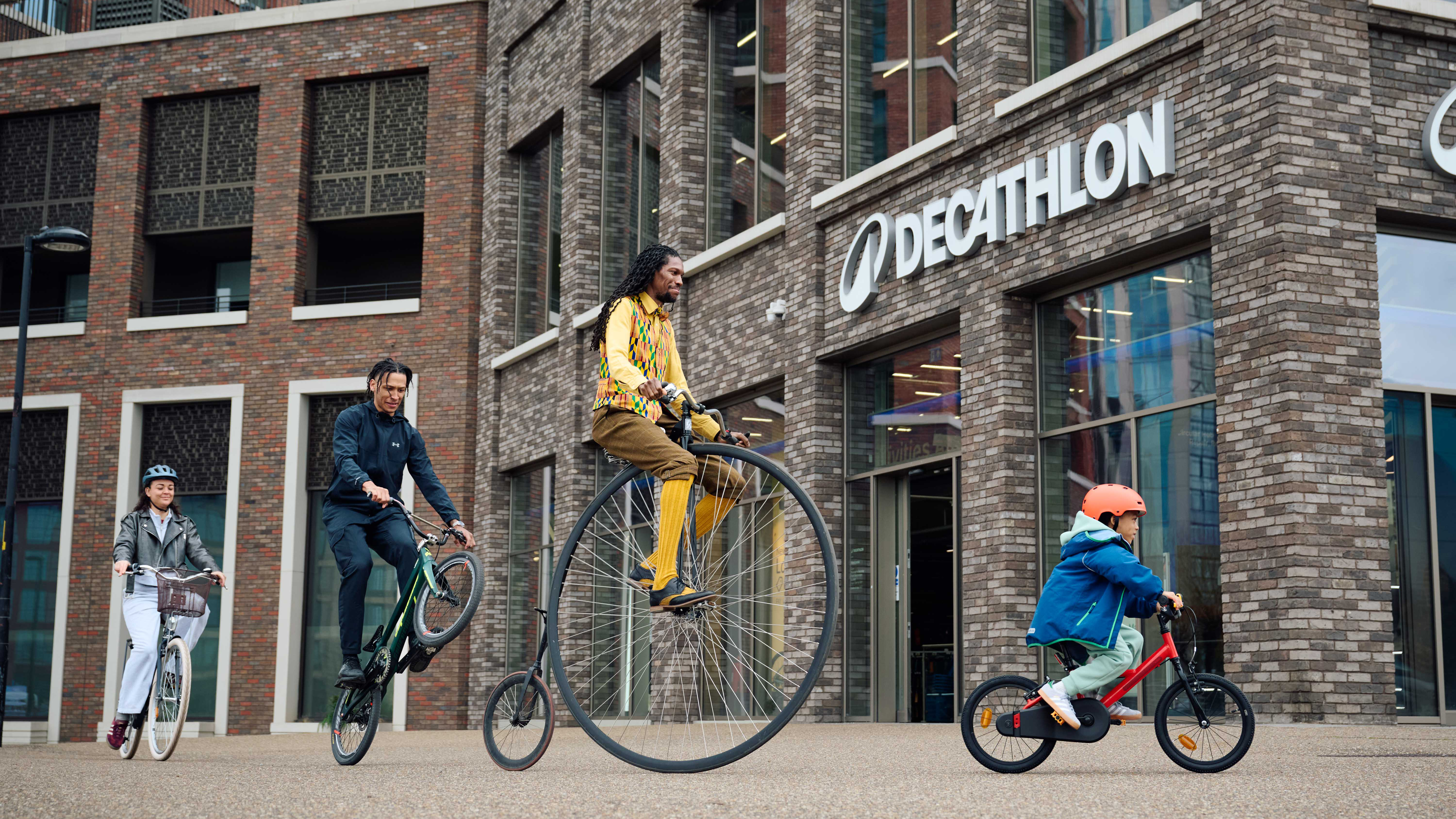 A child, BMXer, lady on a classic style bike and gentlemen on a penny farthing riding into a Decathlon store