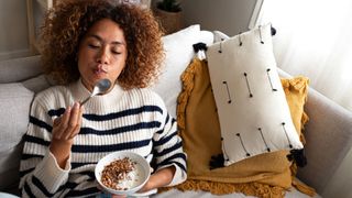 Woman eating bowl of kefir yoghurt sitting on the sofa