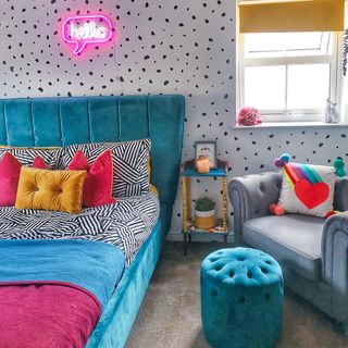 Colourful bedrooom with blue bed, grey couch, blue foot stool and dalmatian patterned wall
