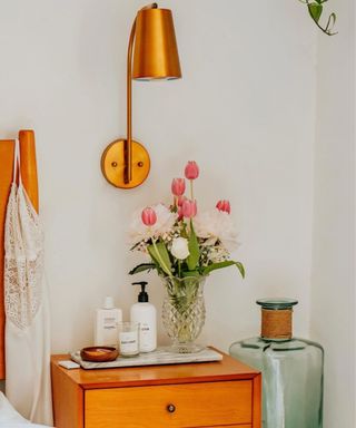 A side table with a vase of tulips on it and a brass lamp above it