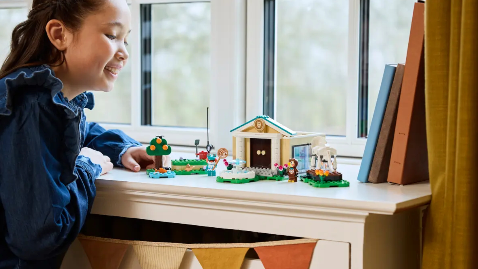 A smiling girl looks down on the Lego Blathers&#039;s Museum Collection set laid out on a white shelf in front of a window