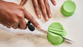 Photo shows a person's hands as they gently slide a knife through a mound of green kinetic sand