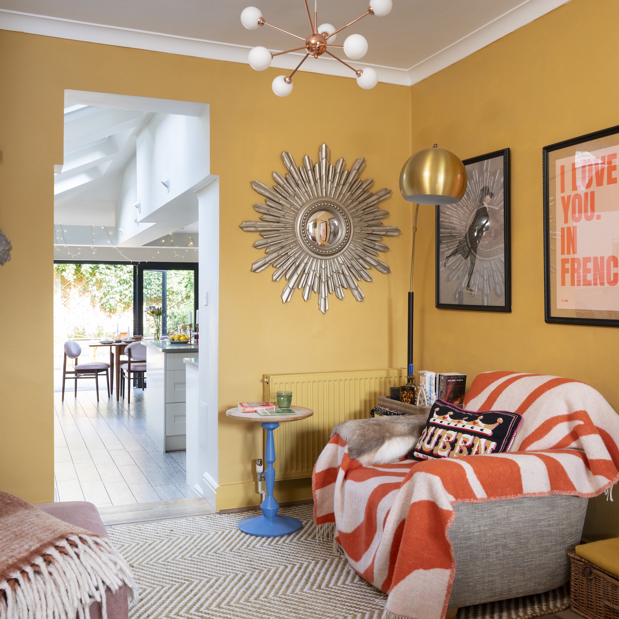 snug sitting room with yellow walls and large starburst mirror on wall, contemporary rug and blue side table