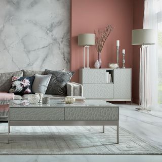 living room with pink and grey designed wall grey sofa with designed cushion and grey table and drawer