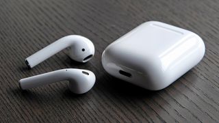 Apple AirPods 2019 på ett bord bredvid sitt tillhörande laddningsfodral.