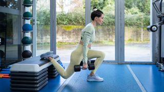 Woman in gym performing a dumbbell Bulgarian split squat