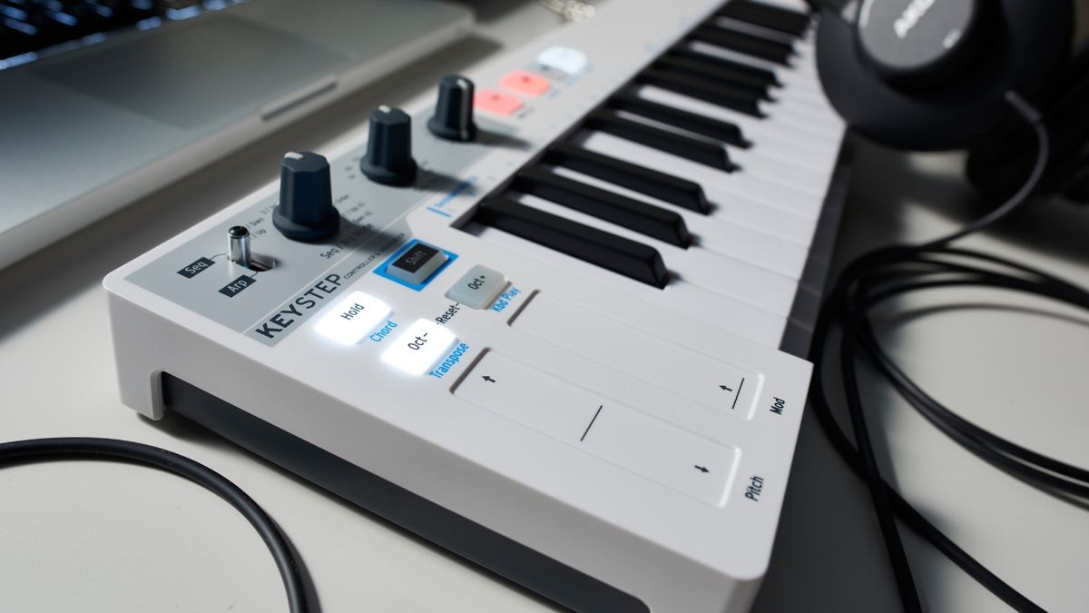 A MIDI keyboard on a desk with a laptop and headphones