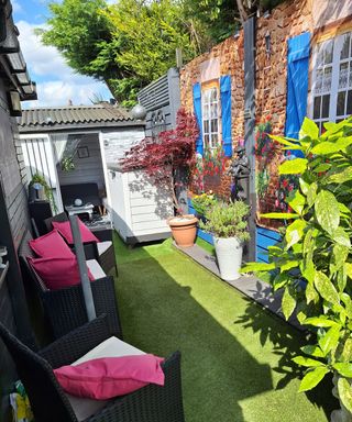A small side garden with a seating area and garden shower curtain attached to a fence with a window and shutter motif