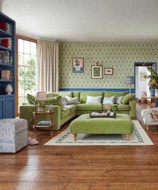 Green velvet sofa and matching ottoman, wood floor, patterned rug and printed green wallapaper