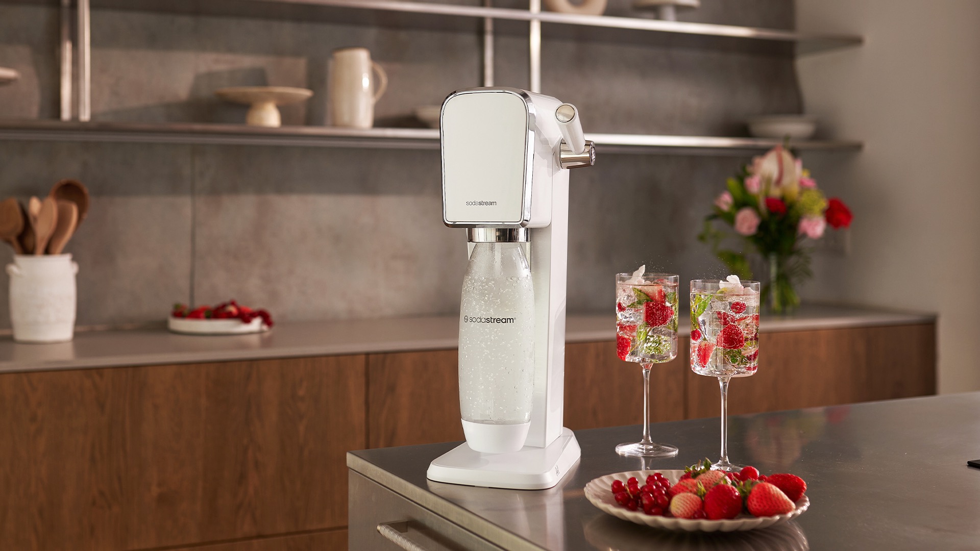 SodaStream Art sparkling water maker, seated on a kitchen countertop next to two glasses of sparkling water filled with strawberries
