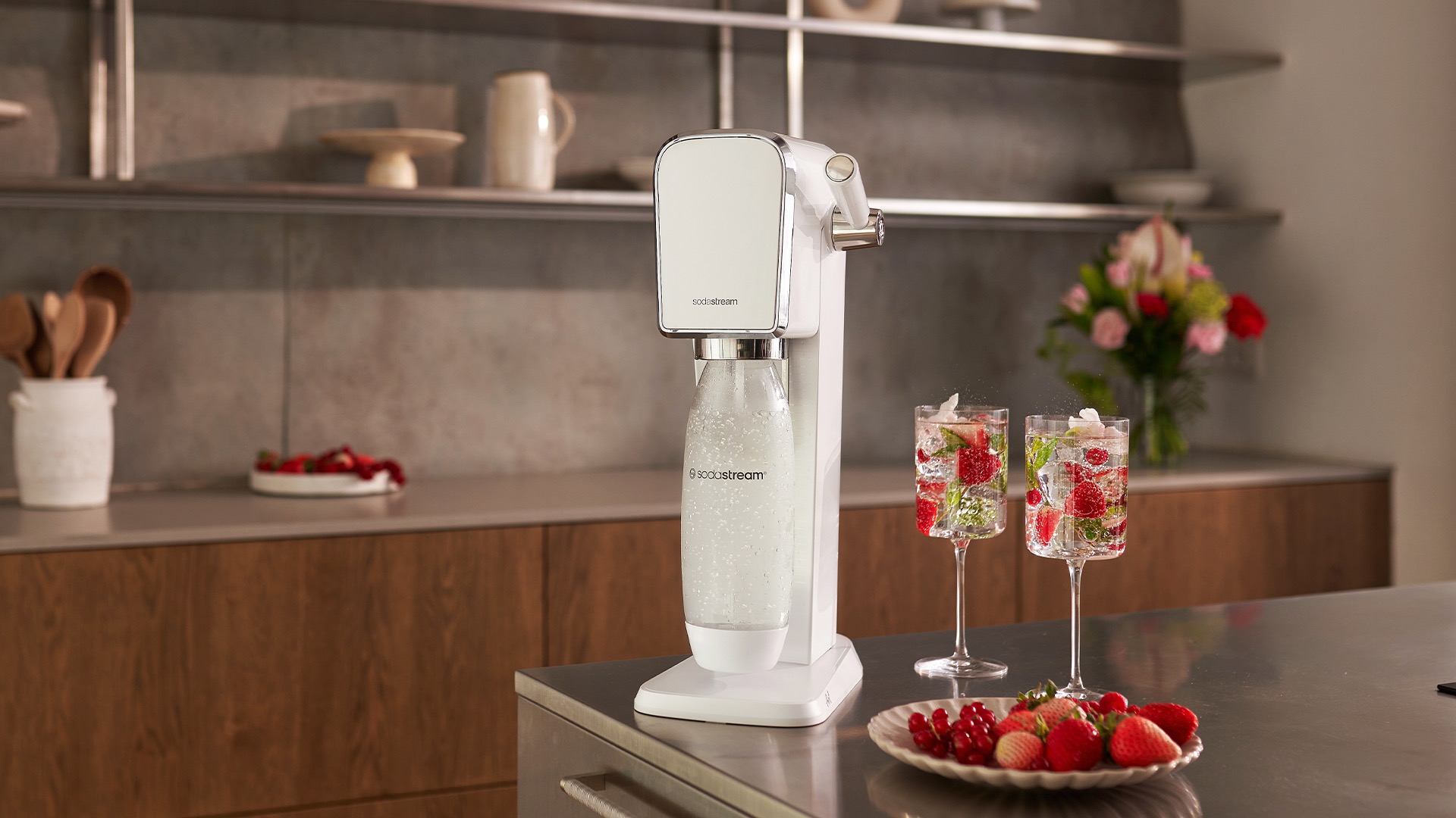 Máquina para hacer agua con gas SodaStream Art, sentada en una mesa de cocina junto a dos vasos de agua con gas llenos de fresas