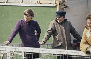 Prince Andrew wears a purple jumper and Princess Anne wears a khaki green jacket and a flat cap