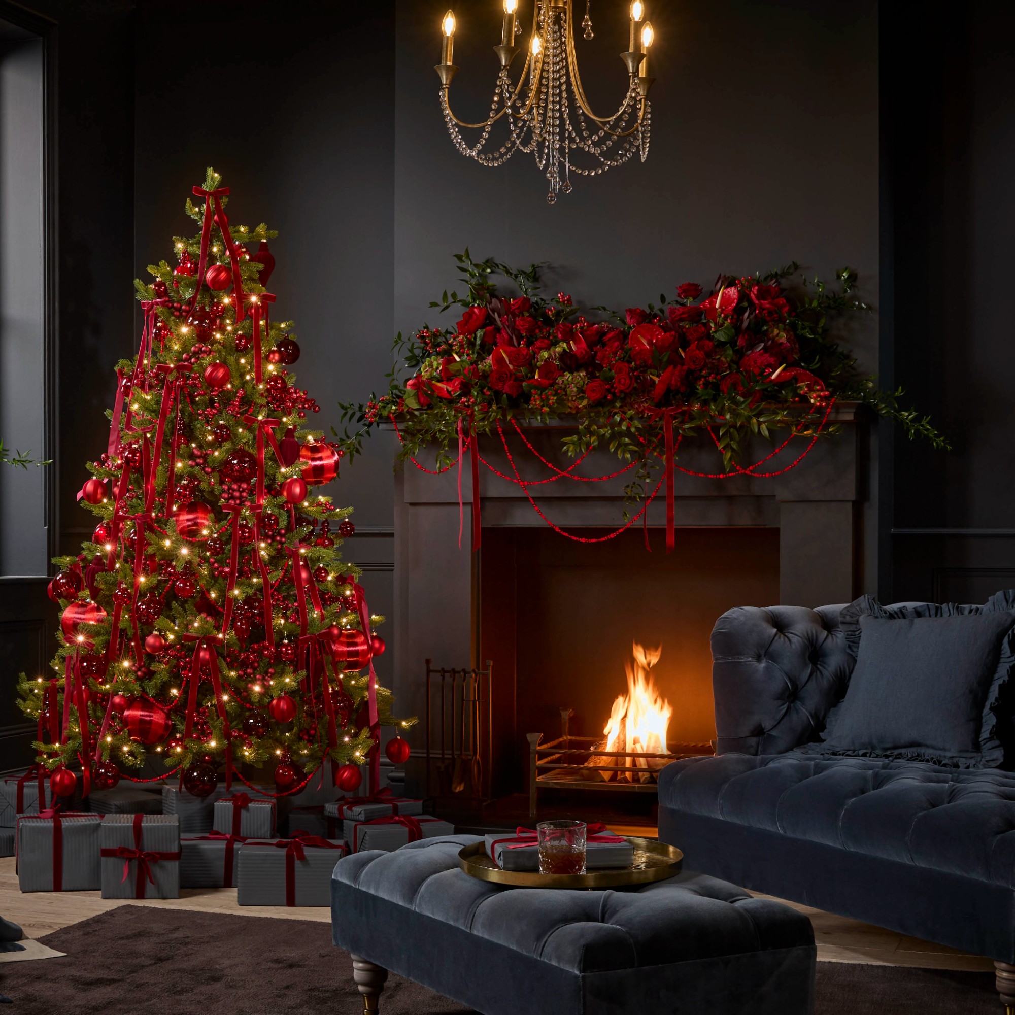 A black-painted living room with dark velvet furniture and a red-decorated Christmas tree and fireplace