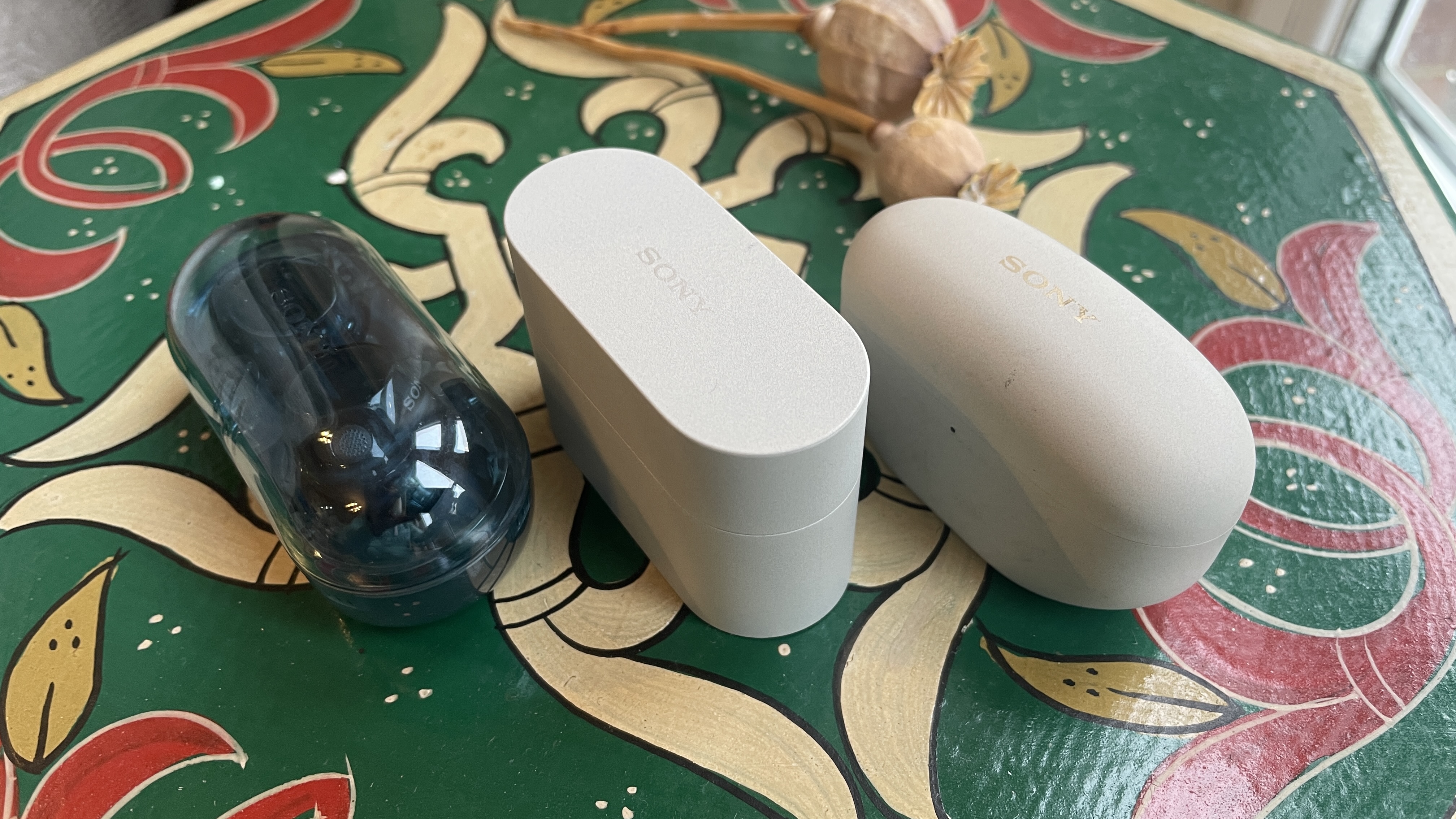 Sony WF-1000XM6 earbuds next to the older-gen. WF-1000XM5 and WF-C710N, on colorful table