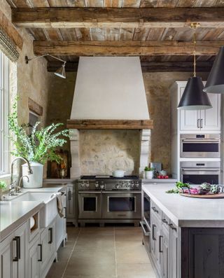 kitchen with white units cooker hood range cooker white island andexposed wooden rafters and stone walls