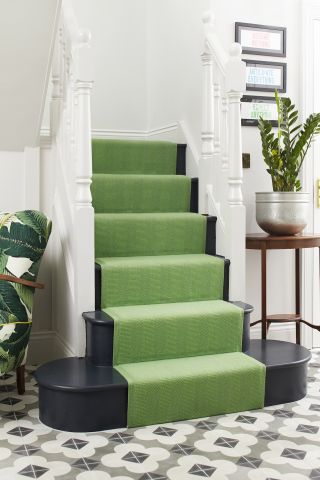 Hallway with geometric patterned floor tiles and black painted stairs with a green runner from Roger Oates