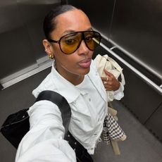 Woman takes an elevator selfie in large aviator sunglasses with yellow-tinted lenses.