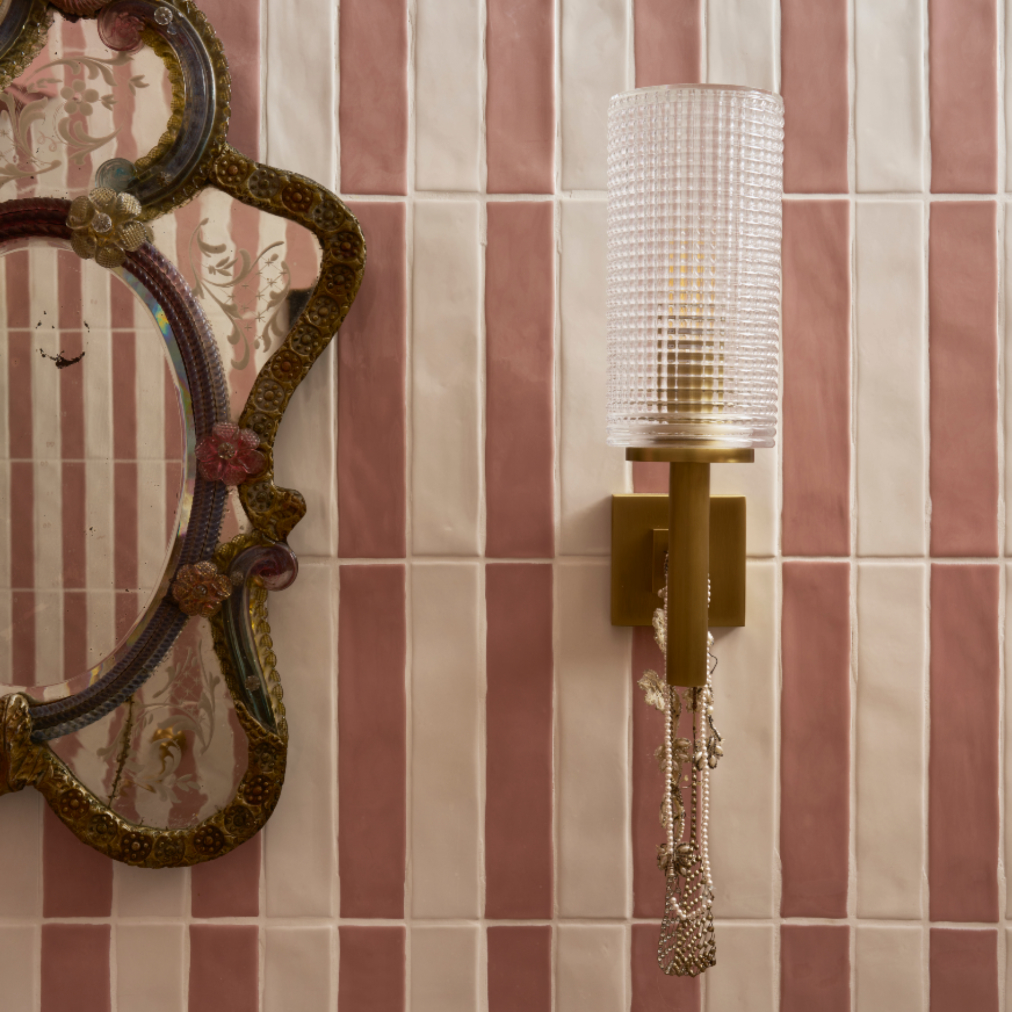 Pearl Lowe's bathroom with pink and white tiles, vintage mirror and brass wall light with glass shade
