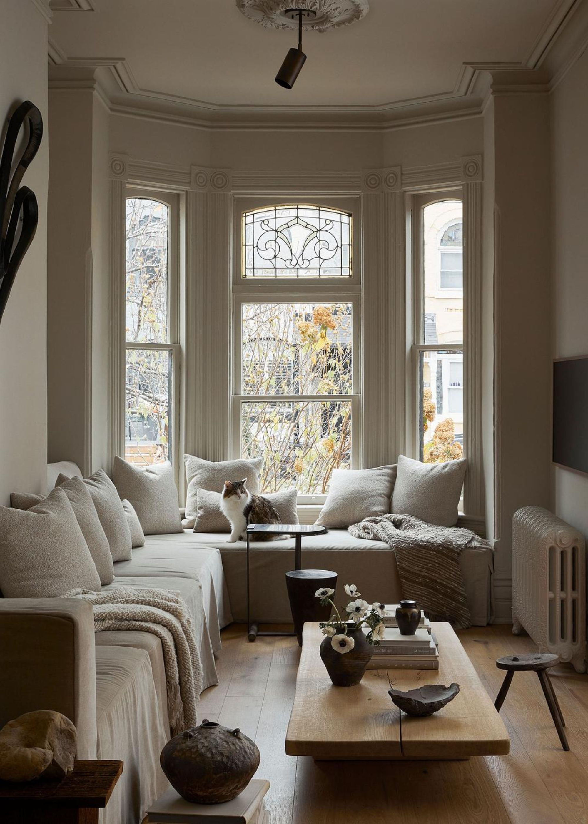 A small living room with a sofa by bay windows and a sofa by the left side of the wall. There is also a view of the coffee table with decor pieces and accessories on top