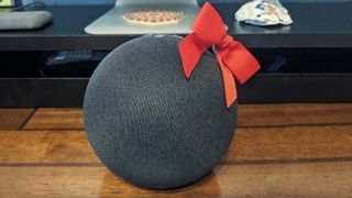 Amazon Echo Dot with a large red bow on top sitting on a wooden table