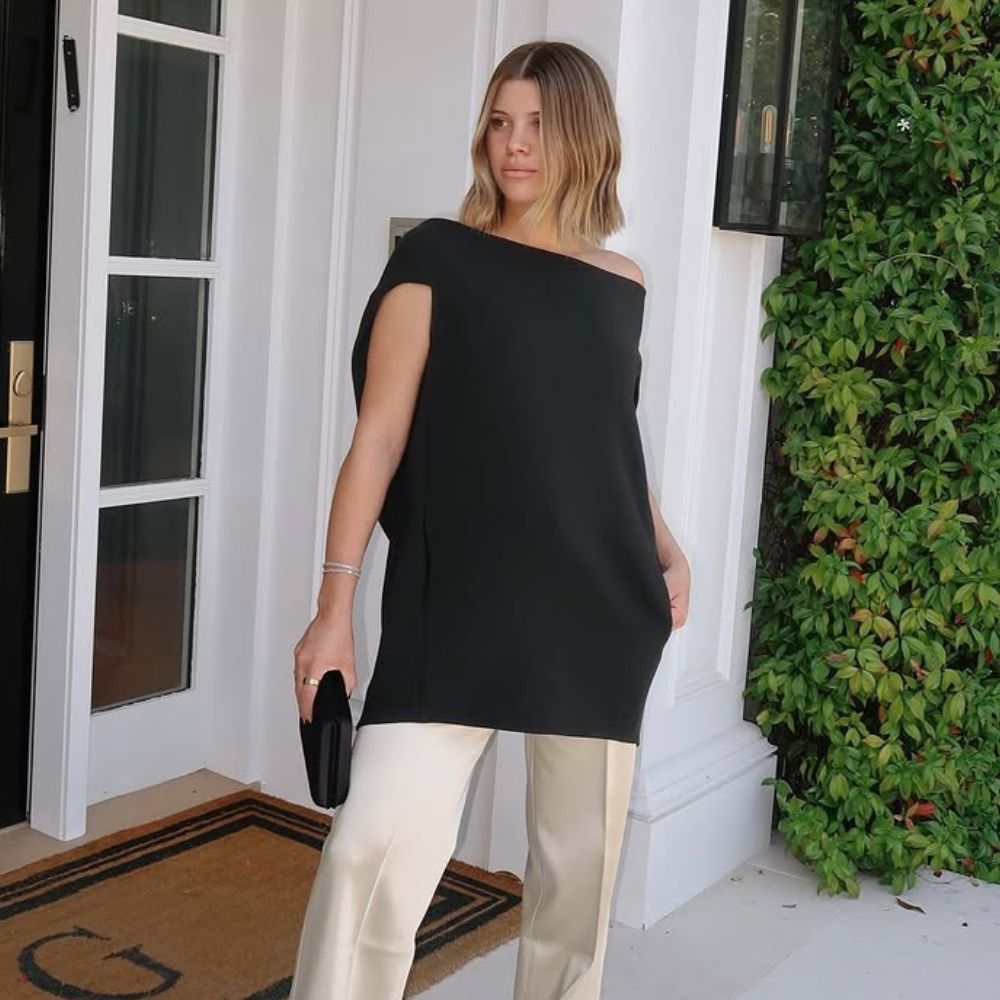 Sofia Richie Grainge posed for a photo wearing a black off-the-shoulder top with cream satin trousers and black chisel toe heels.